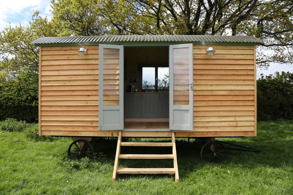 A large wooden shepherd’s hut with French doors and small steps leading up to the entrance.