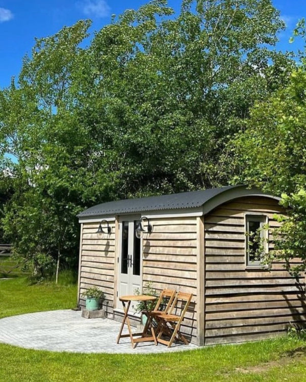 A completed woodern shepherd hut with french doors set in a field.